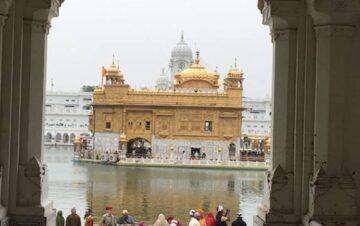 The Golden Temple, also known as Sri Harmandir Sahib, is a magnificent gurdwara located in Amritsar, Punjab, India. The image captures the awe-inspiring beauty of the temple, surrounded by a serene and reflective pool known as the Amrit Sarovar. The temple's golden facade shimmers in the sunlight, showcasing intricate architectural details and ornate decorations. Pilgrims and visitors can be seen walking on the white marble causeway leading to the entrance, embodying a sense of devotion and spirituality. The temple's dome, adorned with a graceful pinnacle, stands tall against the backdrop of a clear blue sky. The Golden Temple is a significant spiritual and cultural landmark, serving as the holiest shrine in Sikhism and a symbol of unity, equality, and peace."