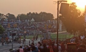 Indian and Pakistani soldiers performing the Wagah Border flag-lowering ceremony at sunset, with crowds cheering in the background."