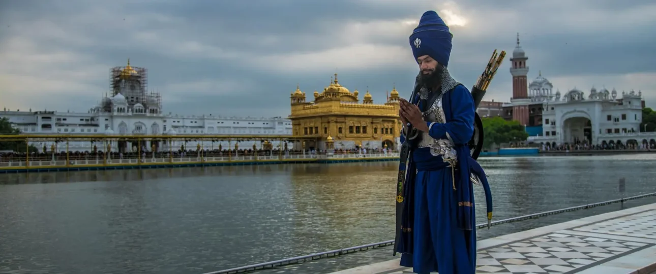 Nihang Sikh standing near the sacred Golden Temple in Amritsar, Punjab, wearing traditional blue attire and turban, symbolizing Sikh valor and heritage.