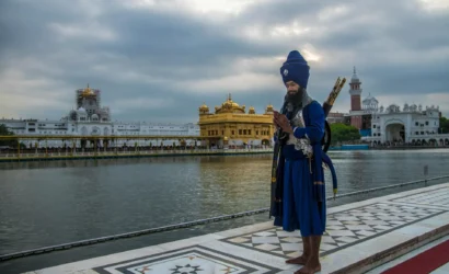 Nihang Sikh standing near the sacred Golden Temple in Amritsar, Punjab, wearing traditional blue attire and turban, symbolizing Sikh valor and heritage.