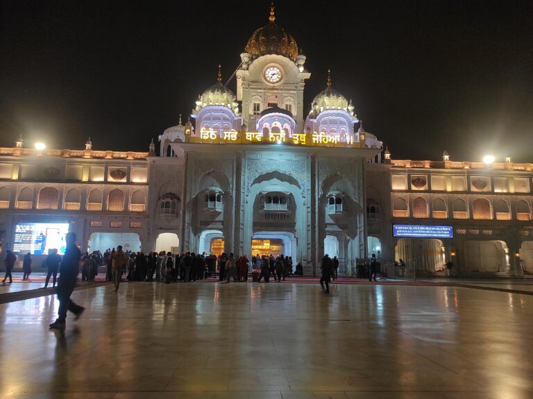 Night view of the illuminated entrance gate of the Golden Temple in Amritsar with a faint glimpse of the shining shrine visible inside the complex.