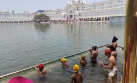 Devotees bathing in the sacred Sarovar at the Golden Temple in Amritsar, with the temple reflected in the calm water during the daytime.