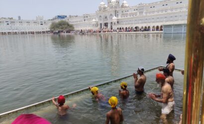 Devotees bathing in the sacred Sarovar at the Golden Temple in Amritsar, with the temple reflected in the calm water during the daytime.